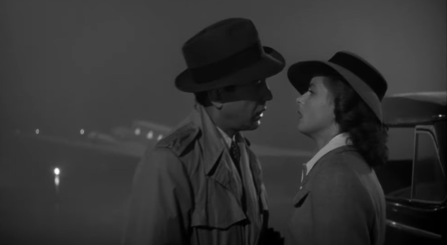 A black and white film still from Casablanca. A man desires a woman: they face either other wearing 1940s hats and clothes looking longingly into each others' eyes.