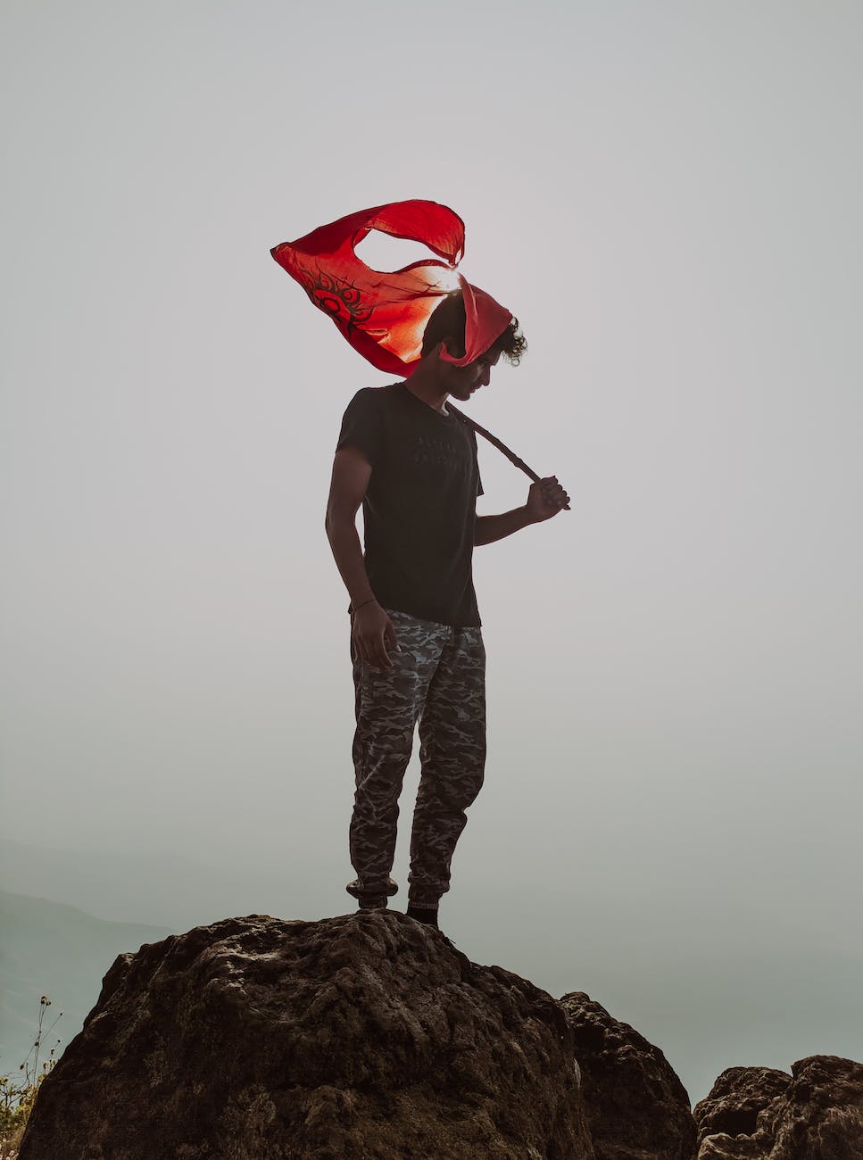 A man stands on a mountain rock, holding a red flag. 