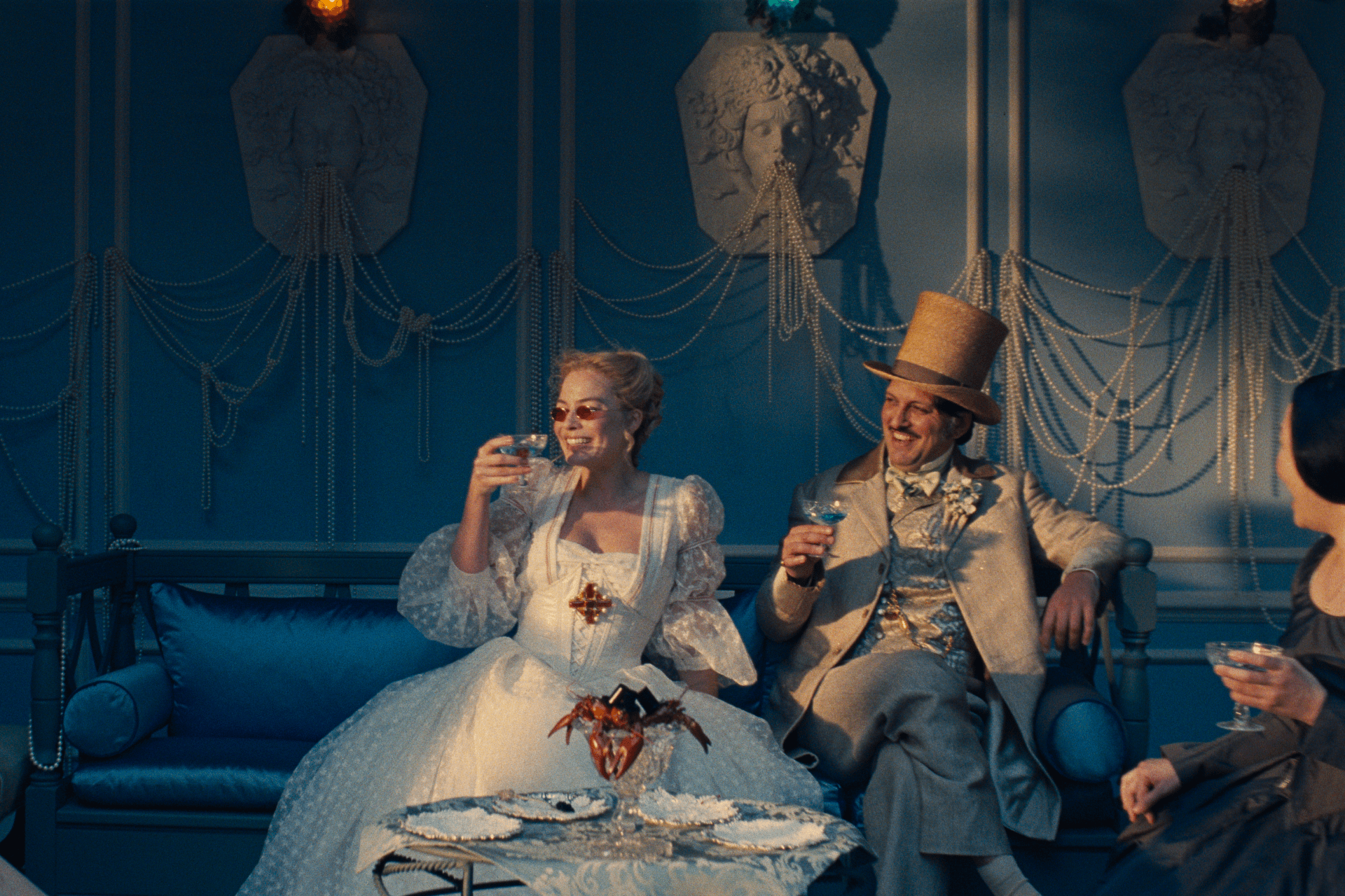 Margot Robbie wears a white dress against a blue background in a still from the film "Wuthering Heights" - for an article by Alex Noel, writer and digital marketer.